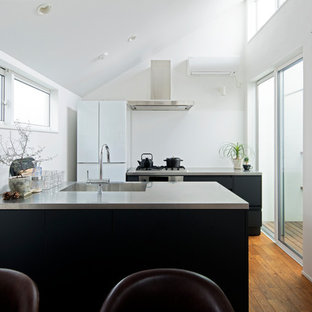 This is an example of a contemporary galley kitchen in Tokyo with an integrated sink, stainless steel benchtops, blue splashback, black appliances, medium hardwood floors, with island, brown floor and blue benchtop.