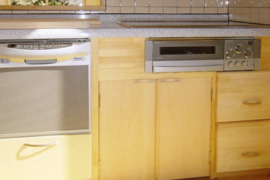 Modelo de cocina lineal de tamaño medio abierta con fregadero integrado, puertas de armario de madera clara, encimera de acrílico, salpicadero de madera, electrodomésticos de acero inoxidable y suelo de madera clara
