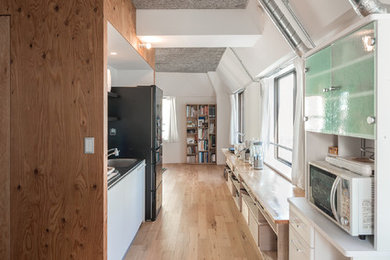 This is an example of a small urban single-wall open plan kitchen in Tokyo with an integrated sink, flat-panel cabinets, white cabinets, stainless steel worktops, white splashback, slate splashback, white appliances, plywood flooring, no island and brown floors.