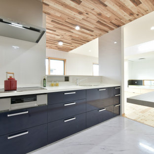 Imagen de cocina lineal, de tamaño medio, abierta, con fregadero bajoencimera, armarios con paneles lisos, puertas de armario azules, encimera de acrílico, salpicadero blanco, salpicadero de vidrio templado, electrodomésticos de acero inoxidable, suelo vinílico, península, suelo blanco, encimeras blancas y papel pintado