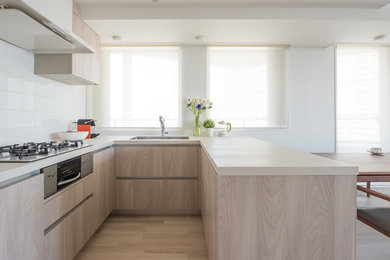 Immagine di una cucina ad U design con lavello sottopiano, ante lisce, ante in legno chiaro, parquet chiaro, penisola, pavimento beige e top beige