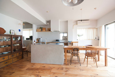 Modelo de cocina comedor rural con salpicadero blanco, electrodomésticos de acero inoxidable, suelo de madera en tonos medios y una isla