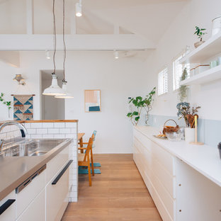 Aménagement d'une cuisine ouverte linéaire scandinave avec un évier encastré, des portes de placard blanches, un plan de travail en inox, une crédence blanche, une crédence en carreau de porcelaine, un sol en contreplaqué, un îlot central et un plan de travail blanc.