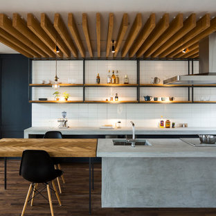 Immagine di una cucina abitabile minimal con lavello sottopiano, nessun'anta, top in cemento, paraspruzzi bianco, paraspruzzi con piastrelle diamantate, parquet scuro e penisola