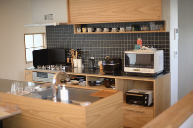 他の地域にある北欧スタイルのおしゃれなキッチン (一体型シンク、フラットパネル扉のキャビネット、茶色いキャビネット、ステンレスカウンター、セラミックタイルのキッチンパネル、シルバーの調理設備、無垢フローリング、茶色い床、グレーのキッチンカウンター) の写真