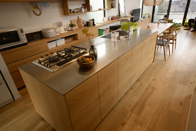 Idées déco pour une cuisine ouverte linéaire scandinave en bois brun avec un évier intégré, un placard à porte plane, un plan de travail en inox, un électroménager en acier inoxydable, un sol en bois brun, îlot, un sol marron et un plan de travail gris.
