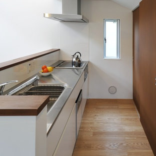 Mid-sized contemporary single-wall open plan kitchen in Tokyo with an integrated sink, flat-panel cabinets, white cabinets, stainless steel benchtops, white splashback, slate splashback, stainless steel appliances, plywood floors and brown floor.