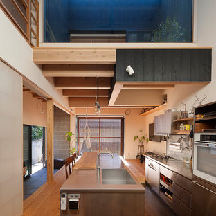 Foto de cocina de galera, de estilo zen, abierta, con suelo de madera clara, fregadero de un seno, armarios con paneles lisos, puertas de armario en acero inoxidable, encimera de acero inoxidable, salpicadero blanco, una isla y suelo marrón