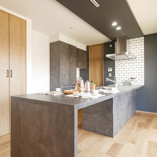 Cette image montre une cuisine ouverte linéaire asiatique avec un évier encastré, un placard à porte affleurante, des portes de placard grises, une crédence blanche, une crédence en carrelage métro, un électroménager en acier inoxydable, un sol en bois clair, une péninsule, un sol beige et un plan de travail gris.