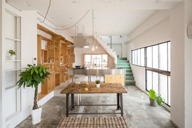 Réalisation d'une salle à manger ouverte sur la cuisine urbaine avec un mur blanc, sol en béton ciré et un sol gris.