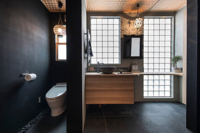 東京23区にあるコンテンポラリースタイルのおしゃれなトイレ・洗面所 (フラットパネル扉のキャビネット、中間色木目調キャビネット、黒い壁、ベッセル式洗面器、木製洗面台、黒い床、ブラウンの洗面カウンター) の写真