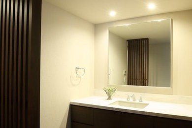 東京23区にあるおしゃれなトイレ・洗面所 (濃色木目調キャビネット、白い壁、アンダーカウンター洗面器、茶色い床、白い洗面カウンター) の写真