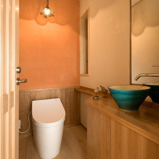 Inspiration pour un WC et toilettes traditionnel avec un placard à porte plane, des portes de placard en bois brun, un mur orange, un sol en bois peint, une vasque et un sol marron.