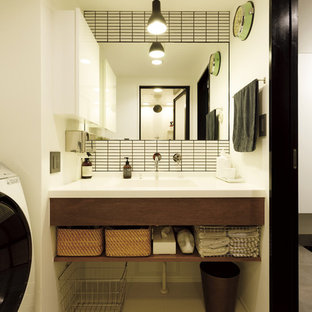 Cette photo montre un WC et toilettes asiatique avec un placard à porte plane, des portes de placard en bois sombre, un carrelage blanc, un mur blanc, un lavabo intégré, un sol beige et un plan de toilette blanc.