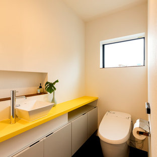 Ispirazione per un bagno di servizio moderno di medie dimensioni con ante bianche, WC monopezzo, pareti bianche, lavabo da incasso, top in superficie solida, pavimento nero, top giallo, soffitto in carta da parati e carta da parati