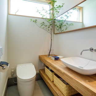 Réalisation d'un WC et toilettes asiatique avec un placard sans porte, des portes de placard en bois brun, un WC à poser, un mur blanc, béton au sol, une vasque, un plan de toilette en bois, un sol gris, un plan de toilette marron et meuble-lavabo suspendu.