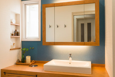 Diseño de aseo mediterráneo con paredes azules, lavabo sobreencimera, encimera de madera y suelo beige