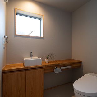 Idées déco pour un WC et toilettes asiatique avec un placard à porte affleurante, des portes de placard en bois brun, un mur bleu, un plan de toilette en bois, un sol blanc et un plan de toilette marron.