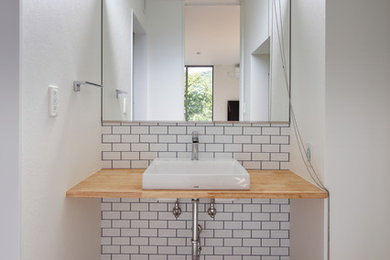 他の地域にある北欧スタイルのおしゃれなトイレ・洗面所 (白いタイル、白い壁、ベッセル式洗面器、木製洗面台、ベージュの床、ブラウンの洗面カウンター) の写真