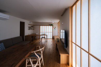 Modelo de sala de estar abierta de estilo zen sin chimenea con paredes blancas, suelo de madera en tonos medios, televisor colgado en la pared y suelo marrón