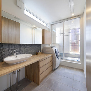 Cette image montre une buanderie urbaine avec un placard à porte plane, des portes de placard en bois clair, un plan de travail en bois, un mur blanc, un sol gris et le lave-linge et le sèche-linge forment un seul appareil électroménager.