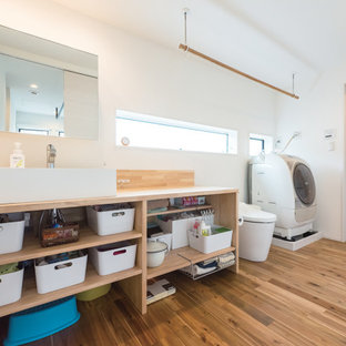 Réalisation d'une buanderie linéaire urbaine multi-usage et de taille moyenne avec un évier posé, un placard sans porte, des portes de placard marrons, un plan de travail en surface solide, un mur blanc, un sol en bois brun, le lave-linge et le sèche-linge forment un seul appareil électroménager, un sol marron et un plan de travail marron.
