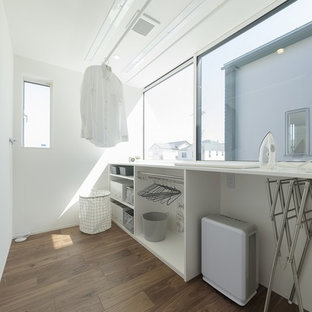Immagine di una sala lavanderia minimalista con pareti bianche, parquet scuro, pavimento marrone e top bianco