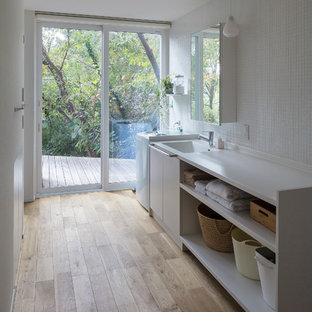Idées déco pour une buanderie linéaire moderne avec un évier intégré, un placard sans porte, des portes de placard blanches, un mur blanc, un sol en bois brun, un sol marron et un plan de travail blanc.