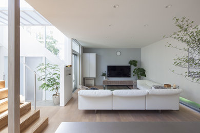 На фото: открытая гостиная комната в стиле модернизм с разноцветными стенами, деревянным полом, телевизором на стене и коричневым полом