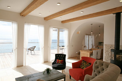 他の地域にある地中海スタイルのおしゃれなLDK (白い壁、薪ストーブ、石材の暖炉まわり、ベージュの床、表し梁) の写真