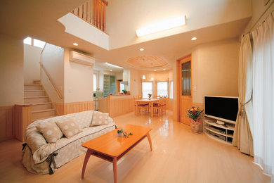 Offenes Wohnzimmer ohne Kamin mit weißer Wandfarbe, Sperrholzboden, freistehendem TV und beigem Boden in Sonstige