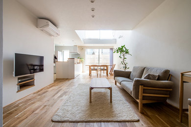 Imagen de salón abierto escandinavo con paredes blancas, suelo de madera clara, televisor colgado en la pared y suelo marrón