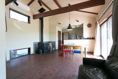 This is an example of an open plan living room in Other with beige walls, dark hardwood flooring, a wood burning stove, a tiled fireplace surround, a freestanding tv and black floors.