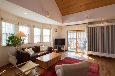 Offenes Wohnzimmer ohne Kamin mit weißer Wandfarbe, braunem Holzboden, freistehendem TV und braunem Boden in Sonstige