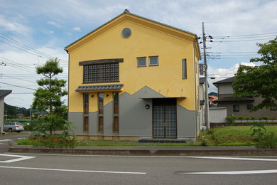 Diseño de fachada amarilla asiática de dos plantas con revestimiento de estuco, tejado a dos aguas y tejado de teja de barro