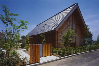 Imagen de fachada marrón asiática de dos plantas con revestimiento de madera y tejado a dos aguas
