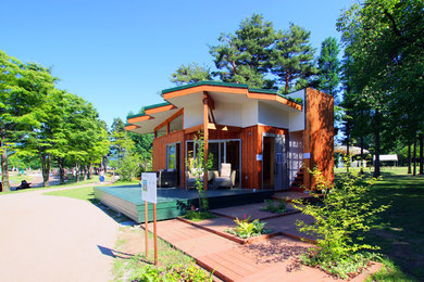 Immagine della facciata di una casa piccola marrone etnica a un piano con tetto a capanna, copertura verde e rivestimento in legno