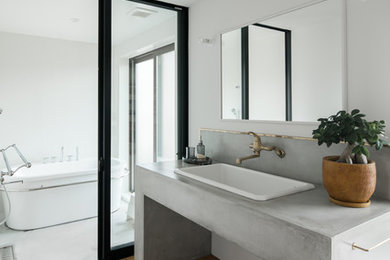 Foto de cuarto de baño principal minimalista con bañera exenta, baldosas y/o azulejos blancos, encimera de cemento, paredes blancas, suelo de madera en tonos medios, lavabo encastrado, suelo marrón y encimeras grises