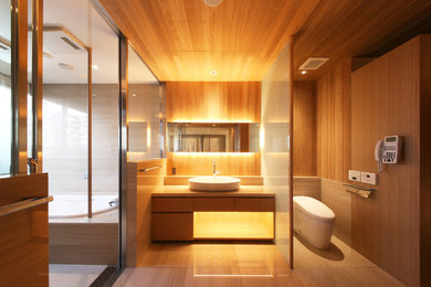 東京都下にあるアジアンスタイルのおしゃれな浴室 (フラットパネル扉のキャビネット、中間色木目調キャビネット、一体型トイレ	、茶色い壁、ベッセル式洗面器、ベージュの床) の写真