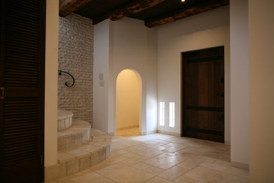 他の地域にある地中海スタイルのおしゃれな玄関ドア (白い壁、ライムストーンの床、茶色いドア、ベージュの床、表し梁) の写真