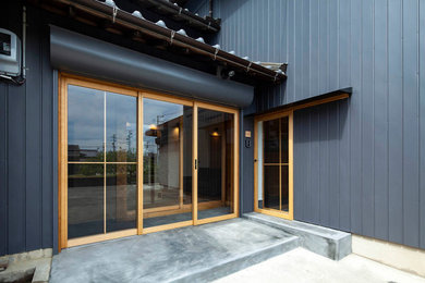他の地域にある小さなアジアンスタイルのおしゃれな玄関ドア (黒い壁、コンクリートの床、淡色木目調のドア、グレーの床) の写真