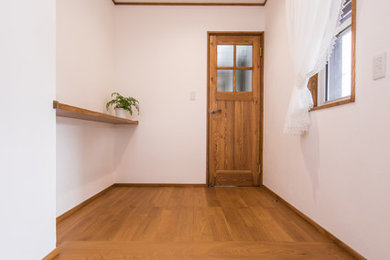 他の地域にあるお手頃価格の小さなカントリー風のおしゃれな玄関ホール (白い壁、無垢フローリング、濃色木目調のドア、茶色い床) の写真