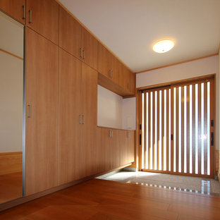 Cette image montre une petit entrée minimaliste avec un couloir, un mur blanc, un sol en contreplaqué, une porte coulissante, une porte en bois brun et un sol marron.