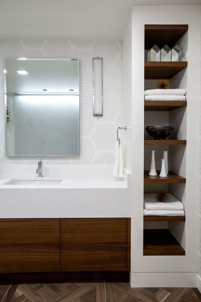 This is an example of a modern master bathroom in Calgary with flat-panel cabinets, brown cabinets, a drop-in tub, a corner shower, a one-piece toilet, white tile, mosaic tile, white walls, porcelain floors, an undermount sink, solid surface benchtops, brown floor, a hinged shower door and white benchtops.