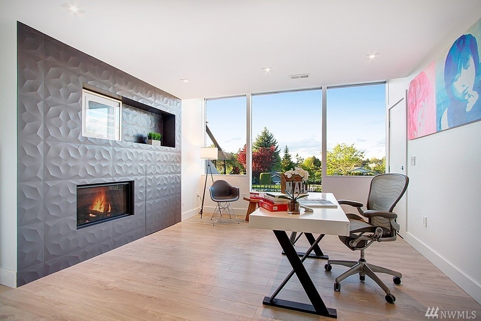 This is an example of a large modern study room in Seattle with grey walls, dark hardwood floors, a standard fireplace, a tile fireplace surround, a freestanding desk and brown floor.