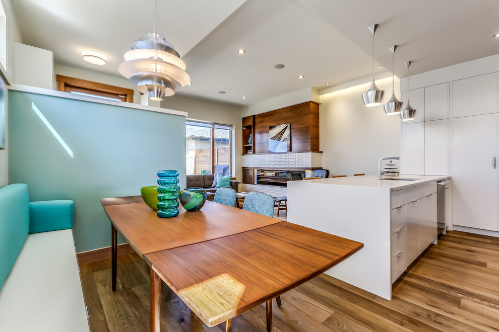 This is an example of a mid-sized midcentury l-shaped eat-in kitchen in Calgary with a single-bowl sink, flat-panel cabinets, white cabinets, quartz benchtops, white splashback, ceramic splashback, stainless steel appliances, medium hardwood floors and a peninsula.