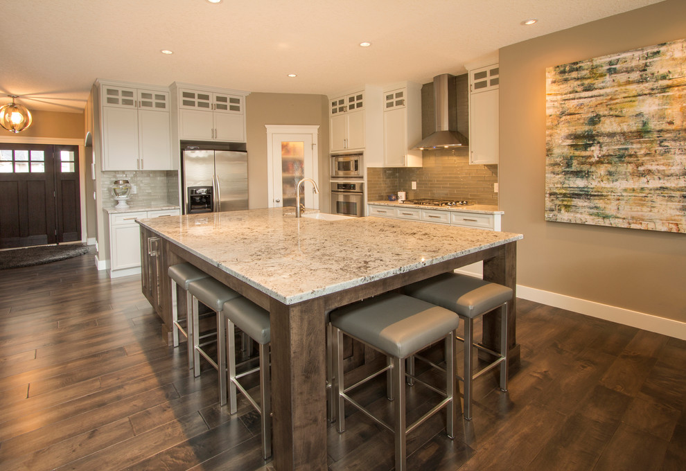 Example of a transitional galley dark wood floor eat-in kitchen design in Calgary with a drop-in sink, shaker cabinets, white cabinets, granite countertops, gray backsplash, glass tile backsplash, stainless steel appliances and an island