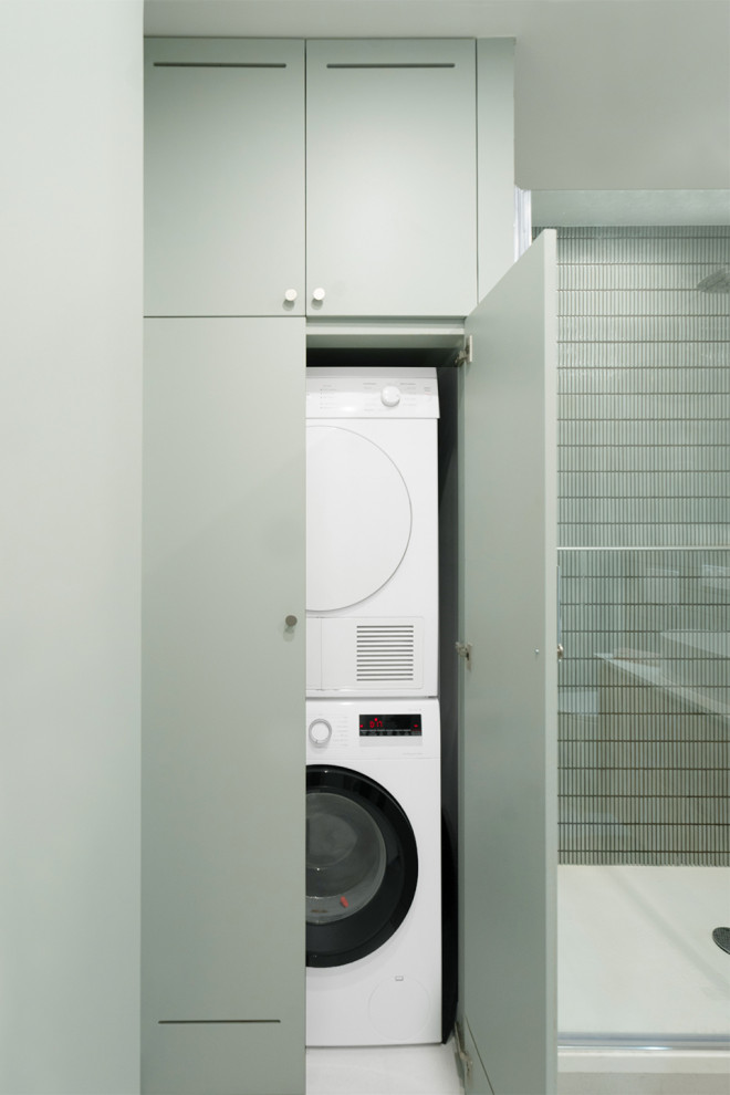 Moderner Hauswirtschaftsraum mit flächenbündigen Schrankfronten, grünen Schränken, grüner Wandfarbe und Waschmaschine und Trockner gestapelt in Paris
