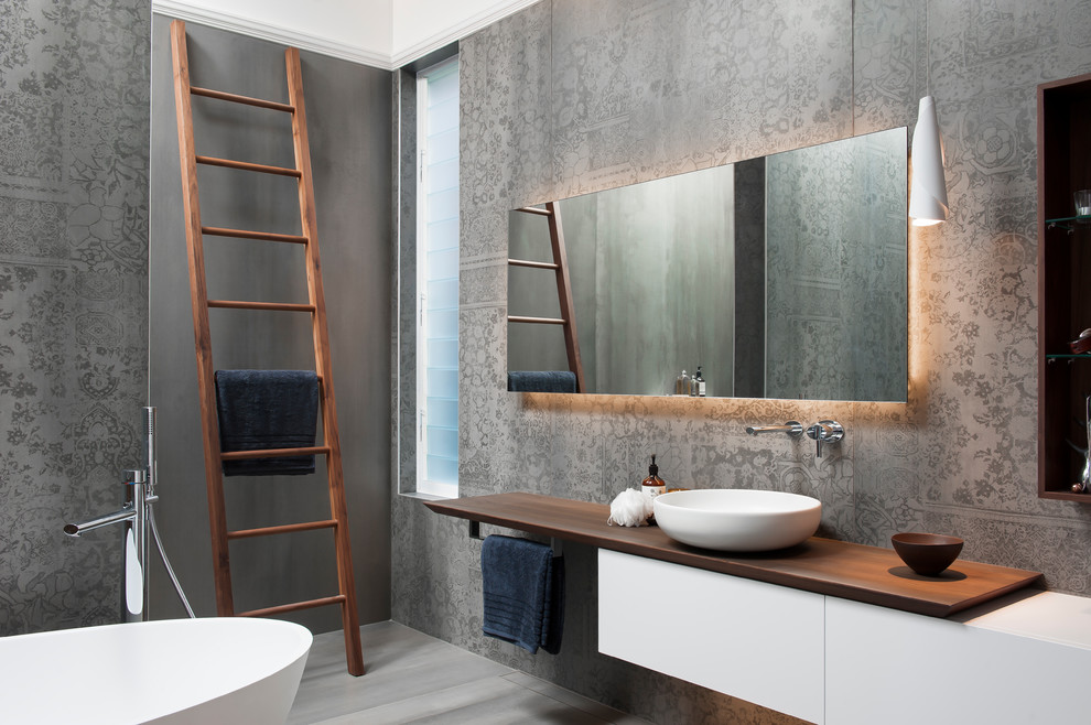 This is an example of a mid-sized modern master wet room bathroom in Sydney with furniture-like cabinets, white cabinets, a freestanding tub, a wall-mount toilet, gray tile, porcelain tile, grey walls, porcelain floors, a vessel sink, wood benchtops, grey floor and an open shower.