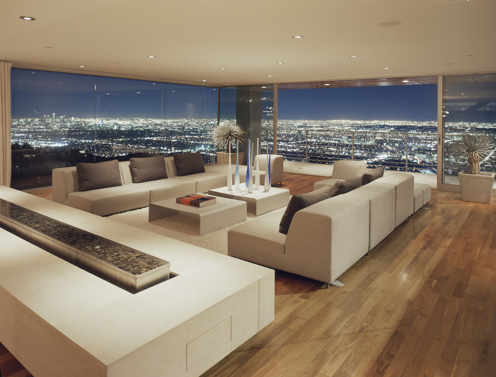 This is an example of an expansive modern formal living room in Los Angeles with a two-sided fireplace, light hardwood floors and a concrete fireplace surround.